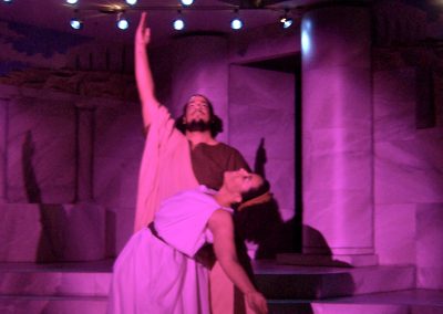 male and female greek figures in a dance pose under pink lights