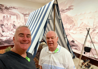 Two men smiling near a striped tent.