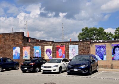 Brick wall of colorful portraits with parked cars